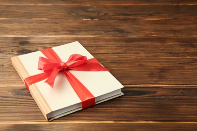 Photo of Book with ribbon as gift on wooden table, space for text