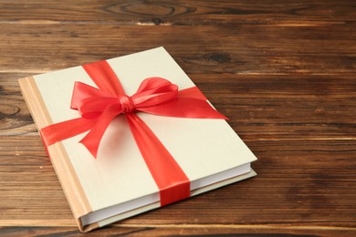 Photo of Book with ribbon as gift on wooden table, space for text