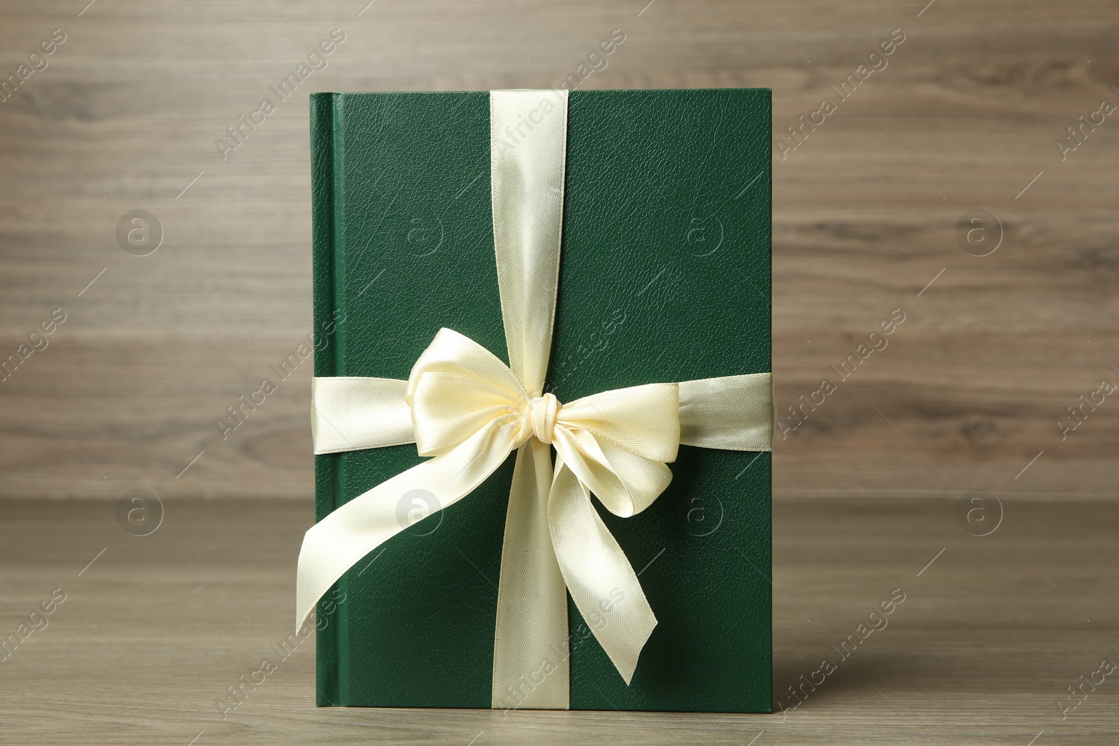 Photo of Book with ribbon as gift on wooden table