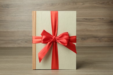 Photo of Book with ribbon as gift on wooden table