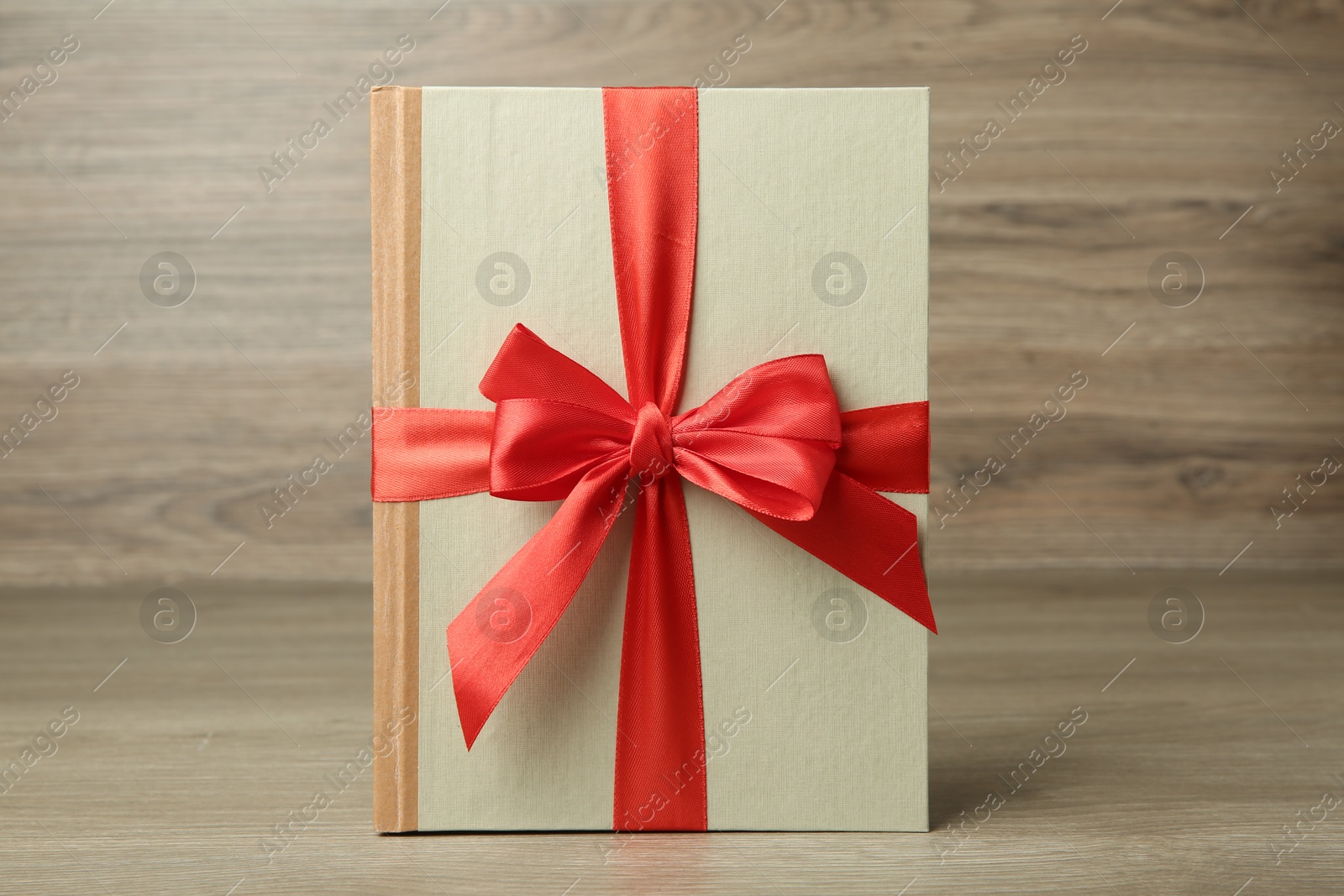 Photo of Book with ribbon as gift on wooden table