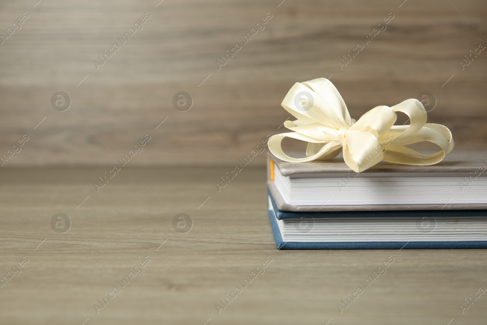 Photo of Books with ribbon as gift on wooden table, space for text