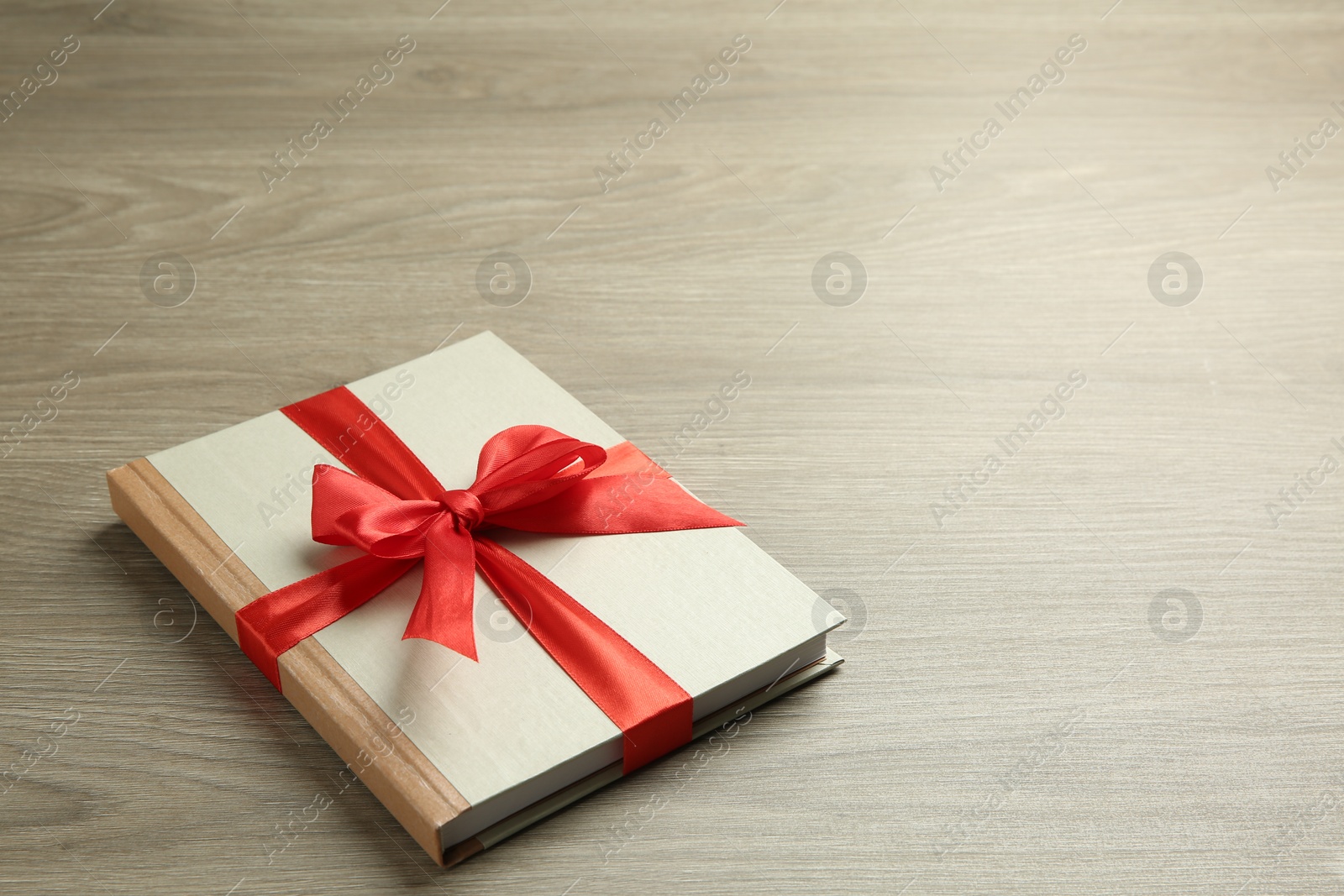 Photo of Book with ribbon as gift on wooden table, space for text