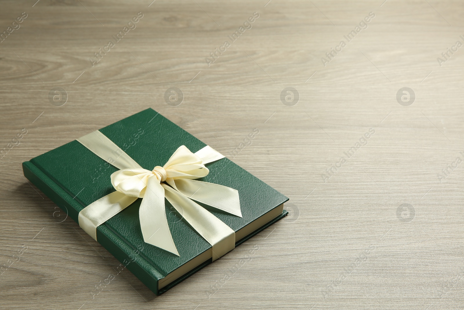 Photo of Book with ribbon as gift on wooden table, space for text