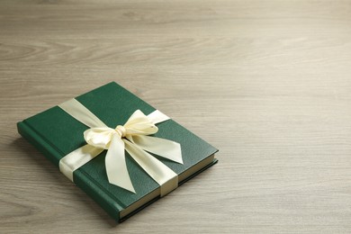 Photo of Book with ribbon as gift on wooden table, space for text