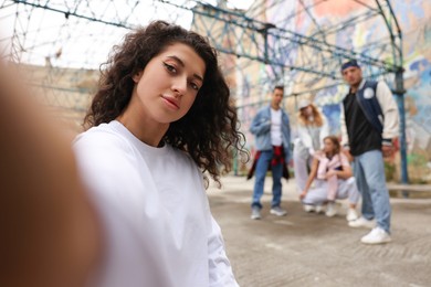 Young woman taking selfie with group of people outdoors, selective focus. Hip hop dancers