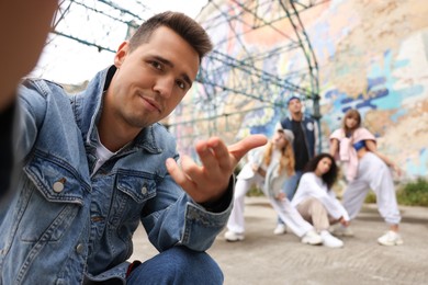 Young man taking selfie with group of people outdoors, selective focus. Hip hop dancers