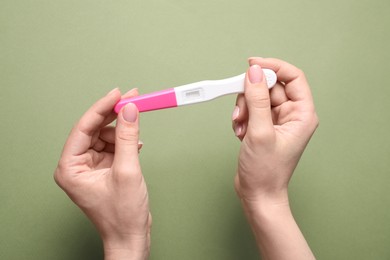 Photo of Woman holding pregnancy test on olive background, top view