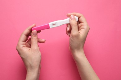 Photo of Woman holding pregnancy test on pink background, top view