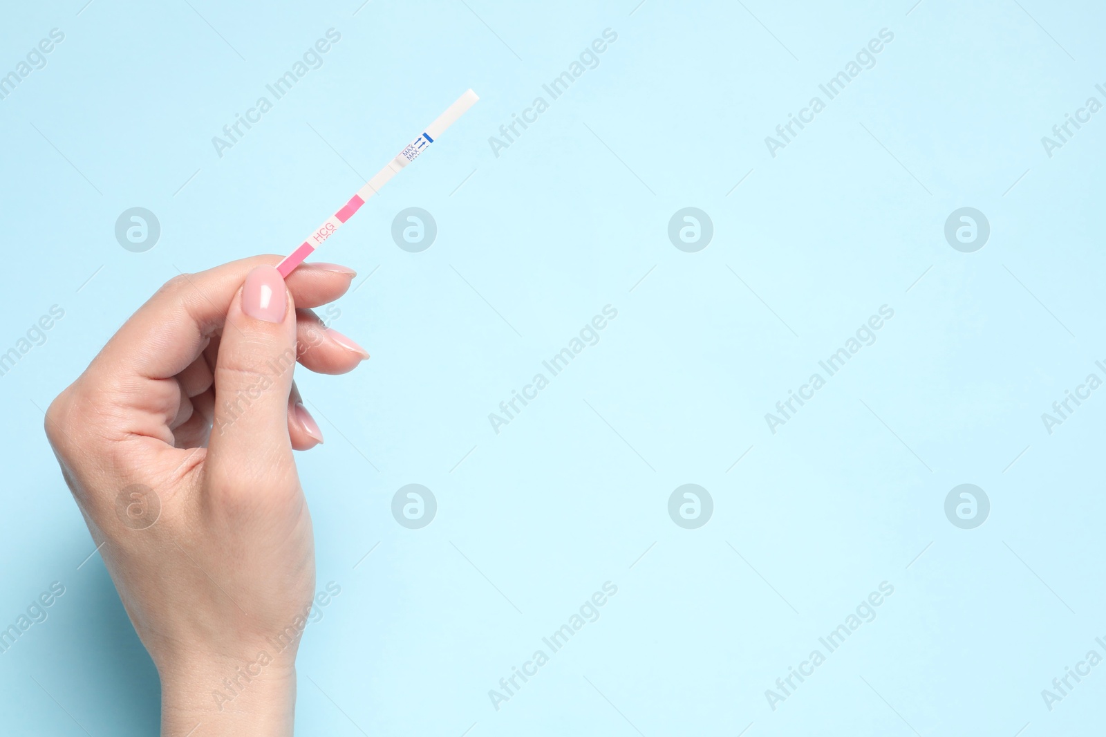 Photo of Woman holding pregnancy test on light blue background, top view. Space for text