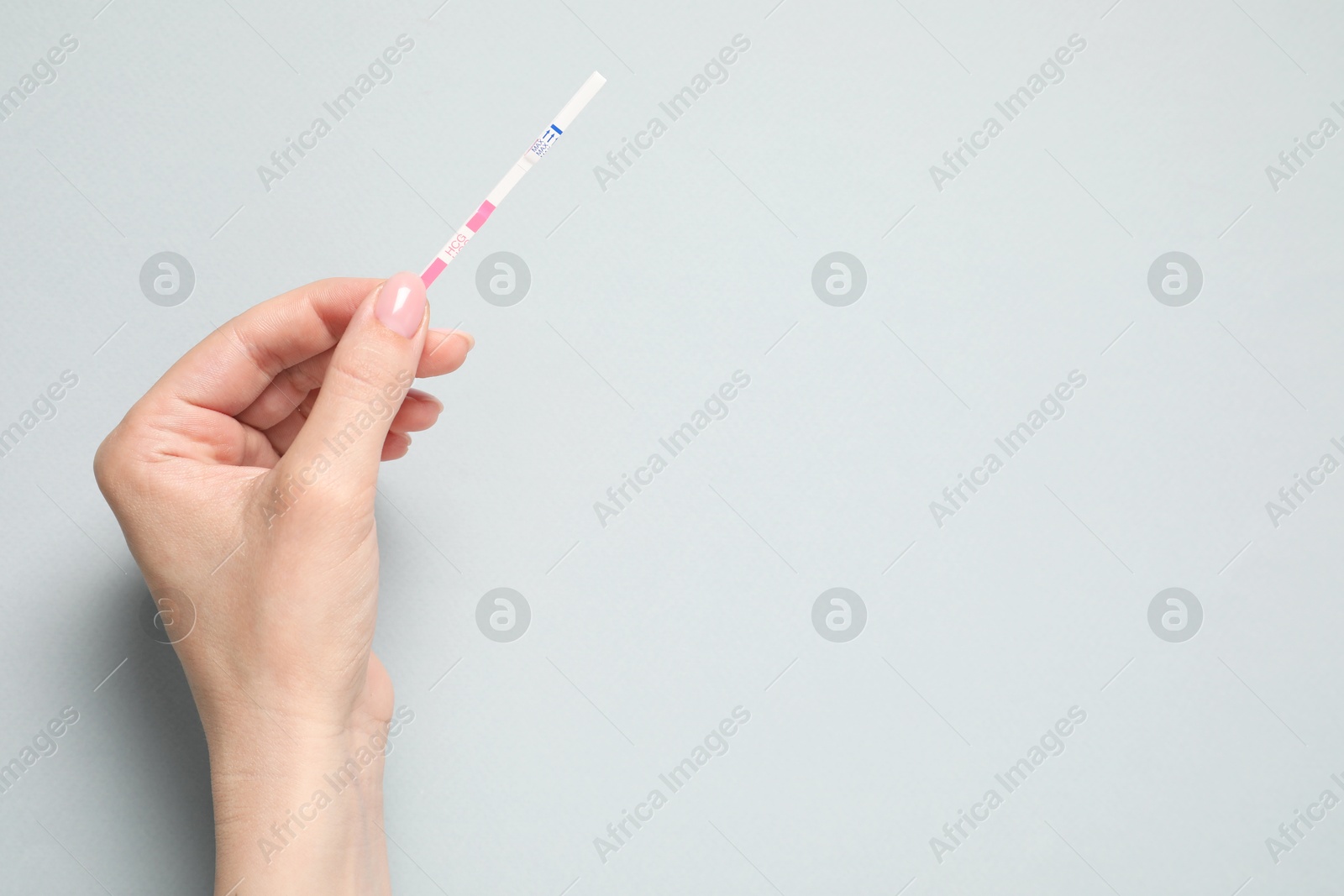 Photo of Woman holding pregnancy test on light grey background, top view. Space for text