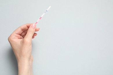 Photo of Woman holding pregnancy test on light grey background, top view. Space for text