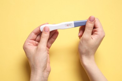 Photo of Woman holding pregnancy test on yellow background, top view