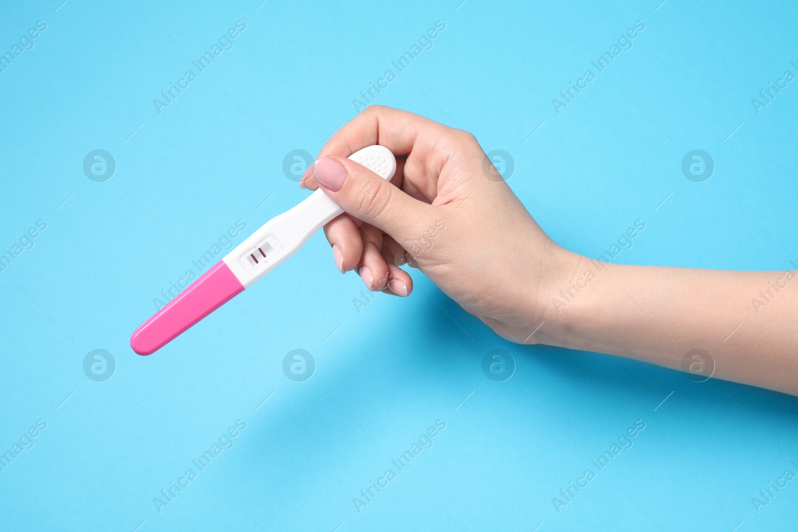 Photo of Woman holding pregnancy test on light blue background, top view