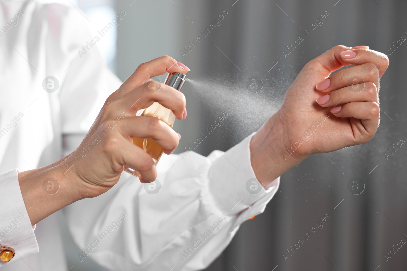 Photo of Woman spraying perfume onto wrist indoors, closeup