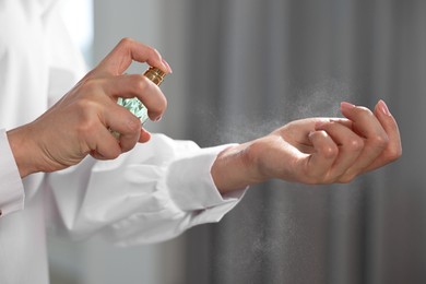 Woman spraying perfume onto wrist indoors, closeup