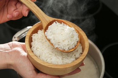 Photo of Woman taking boiled rice from pot into bowl, closeup