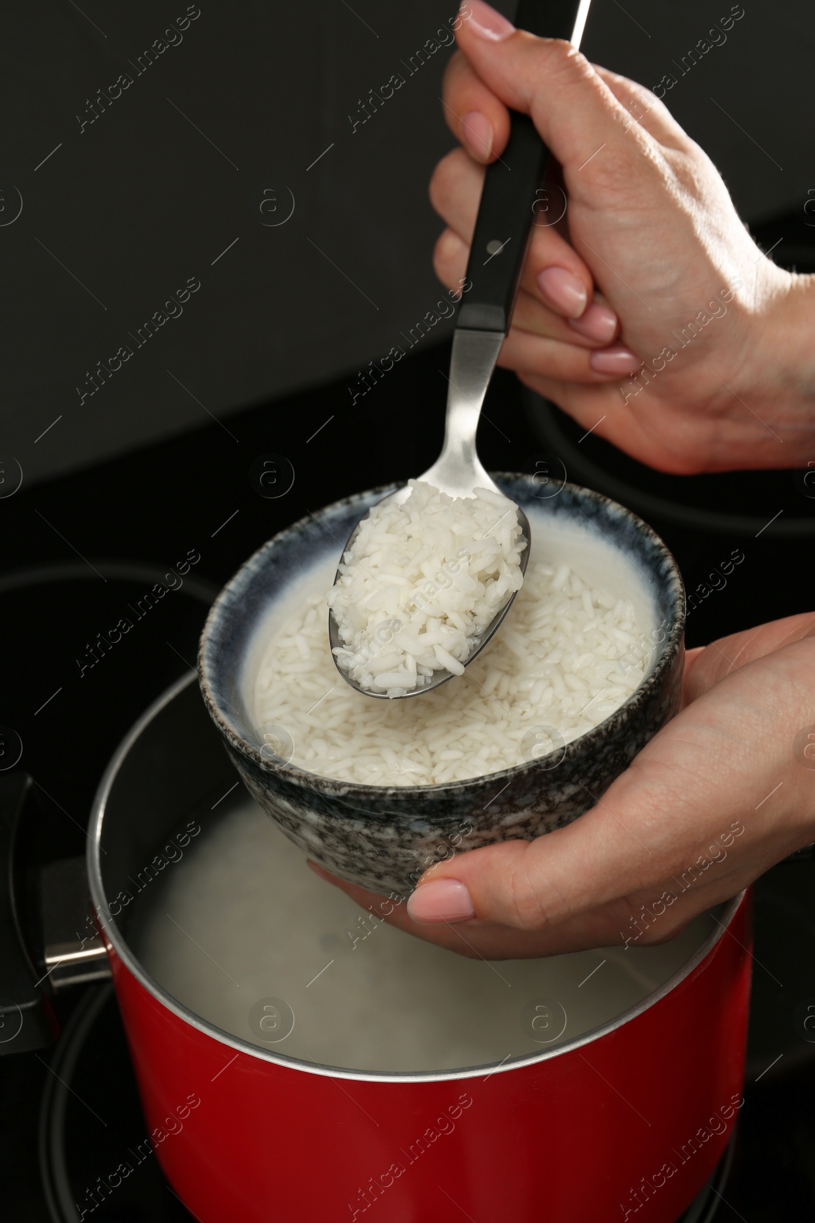 Photo of Woman taking boiled rice from pot into bowl, closeup