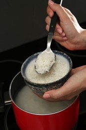 Photo of Woman taking boiled rice from pot into bowl, closeup