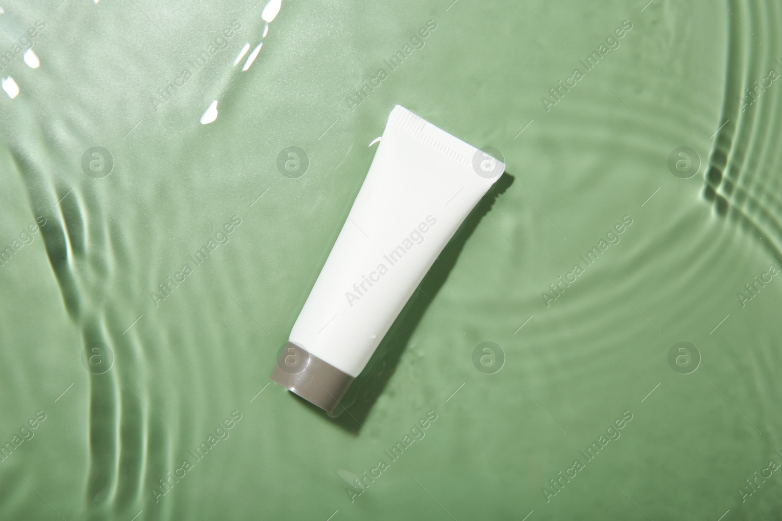 Photo of Tube with cream in water on light green background, top view. Cosmetic product