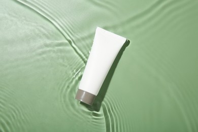 Tube with cream in water on light green background, top view. Cosmetic product