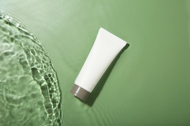 Photo of Tube with cream in water on light green background, top view. Cosmetic product