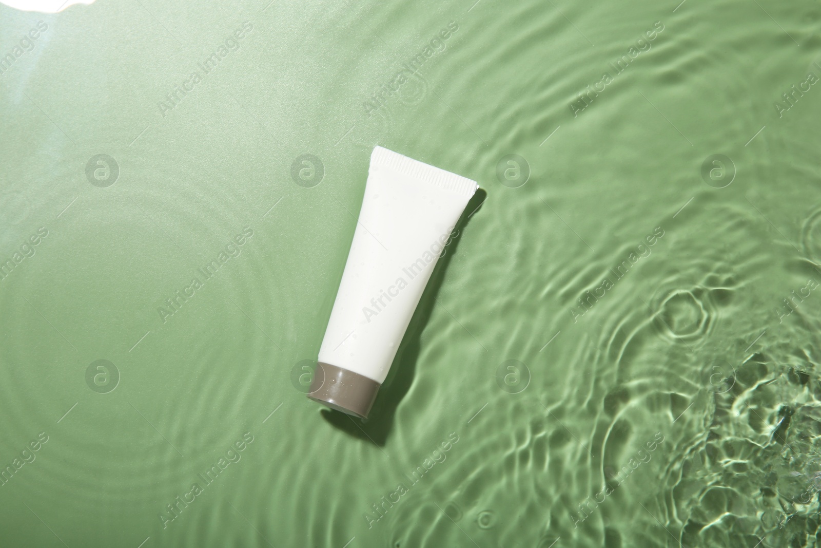 Photo of Tube with cream in water on light green background, top view. Cosmetic product