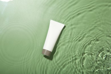 Tube with cream in water on light green background, top view. Cosmetic product