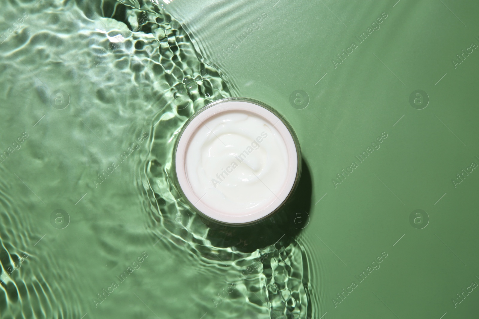 Photo of Jar with cream in water on light green background, top view. Cosmetic product