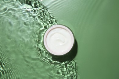 Jar with cream in water on light green background, top view. Cosmetic product