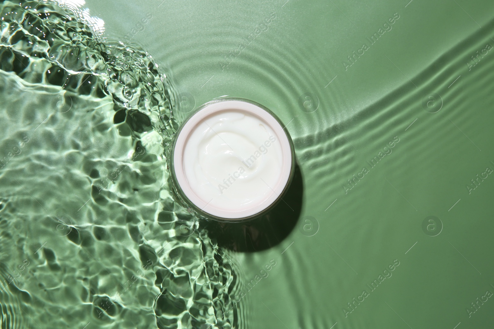 Photo of Jar with cream in water on light green background, top view. Cosmetic product