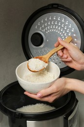 Photo of Woman taking boiled rice into bowl on grey background, closeup