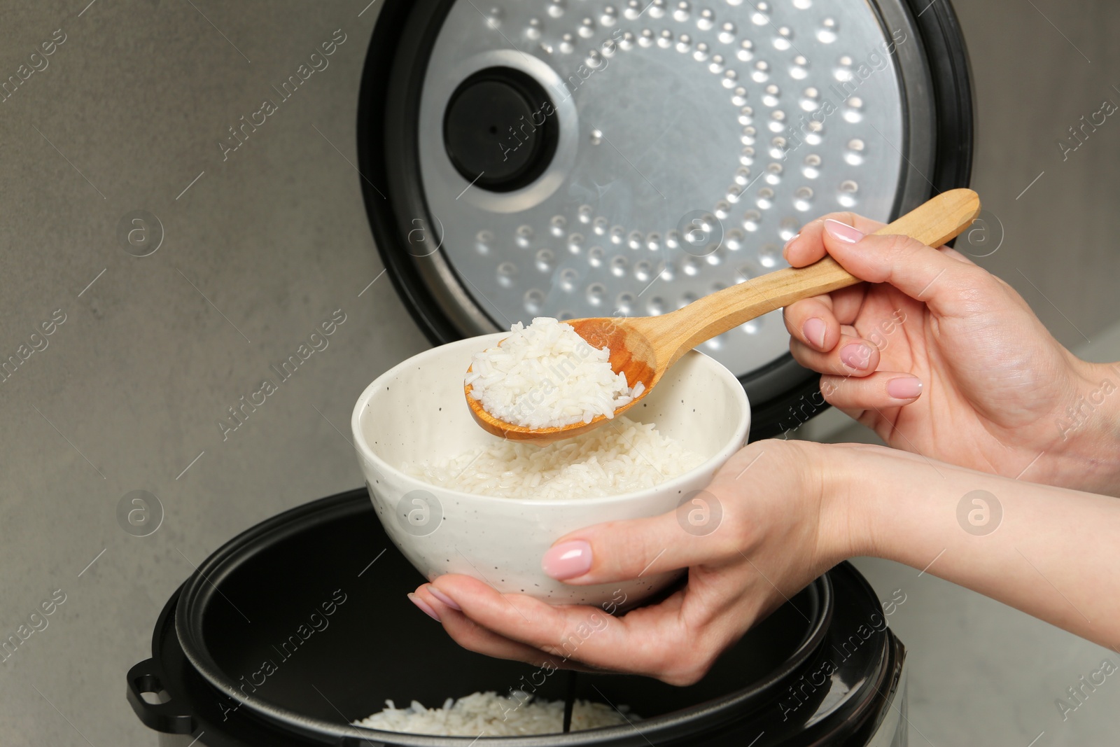 Photo of Woman taking boiled rice into bowl on grey background, closeup