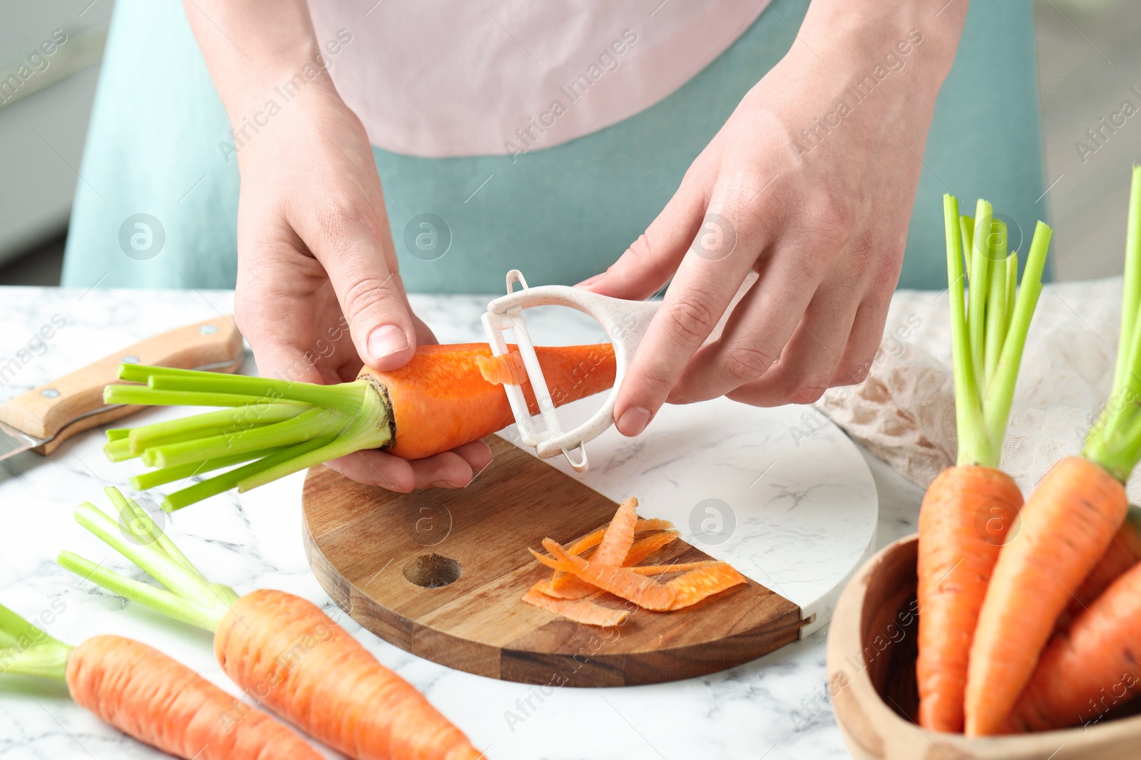 Photo of Woman peeling fresh carrot at white marble table, closeup