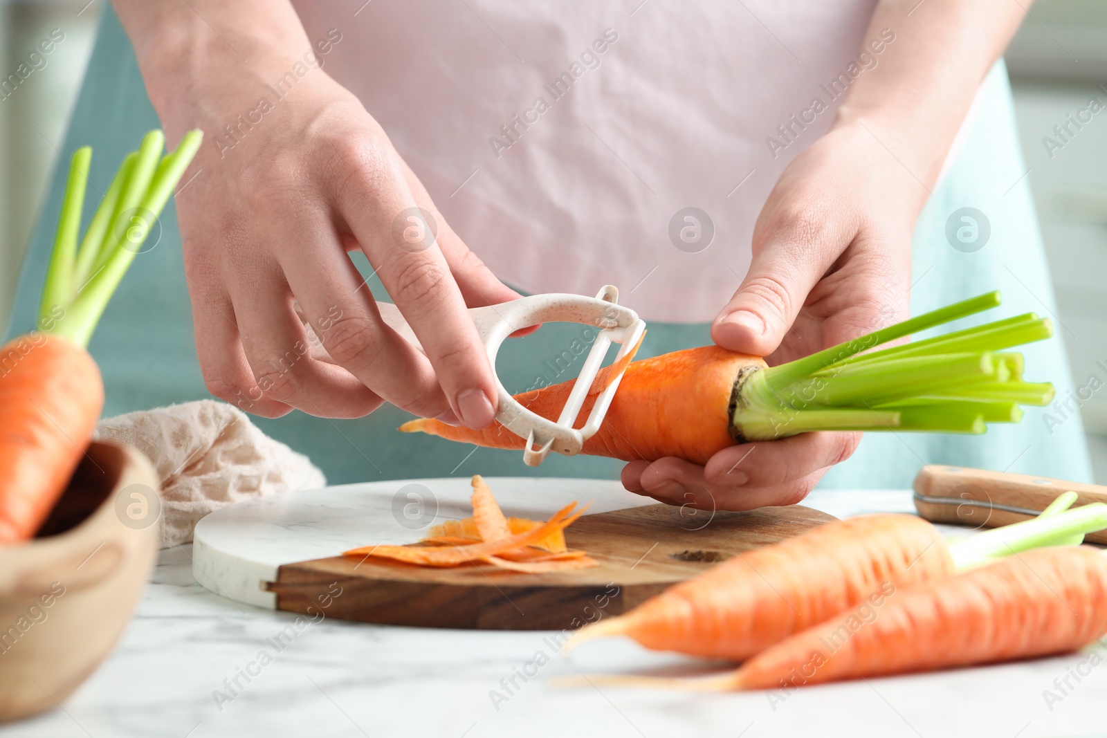 Photo of Woman peeling fresh carrot at white marble table, closeup