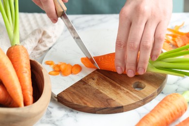 Photo of Woman cutting fresh carrot at white marble table, closeup