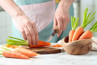 Photo of Woman cutting fresh carrot at white marble table, closeup