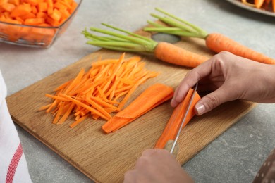 Photo of Woman cutting fresh carrot at gray textured table, closeup