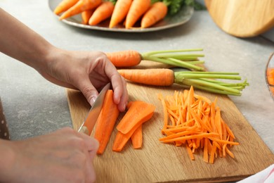 Photo of Woman cutting fresh carrot at gray textured table, closeup