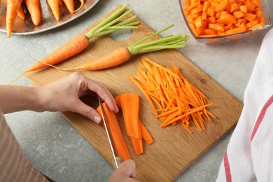 Woman cutting fresh carrot at gray textured table, top view