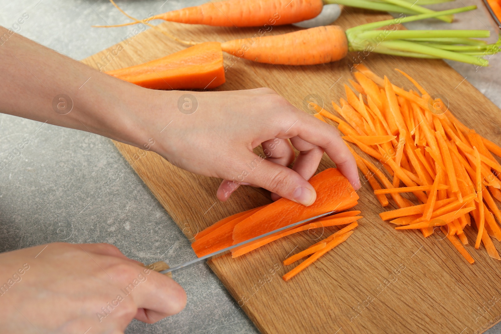 Photo of Woman cutting fresh carrot at gray textured table, closeup