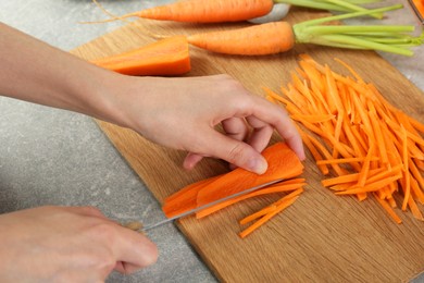 Photo of Woman cutting fresh carrot at gray textured table, closeup