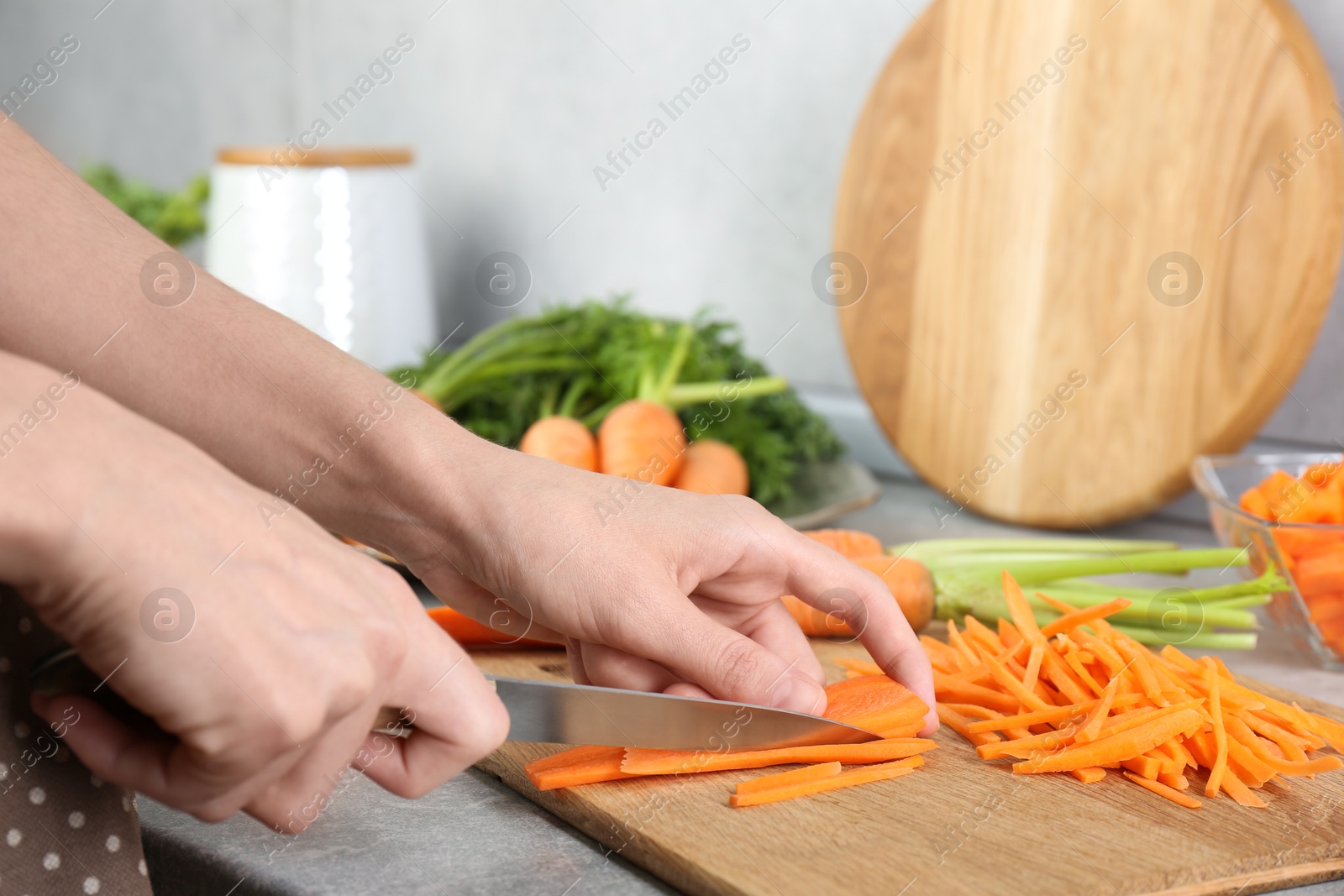 Photo of Woman cutting fresh carrot at gray textured table, closeup