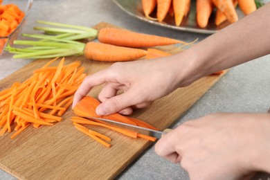 Photo of Woman cutting fresh carrot at gray textured table, closeup