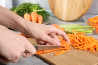 Photo of Woman cutting fresh carrot at gray textured table, closeup