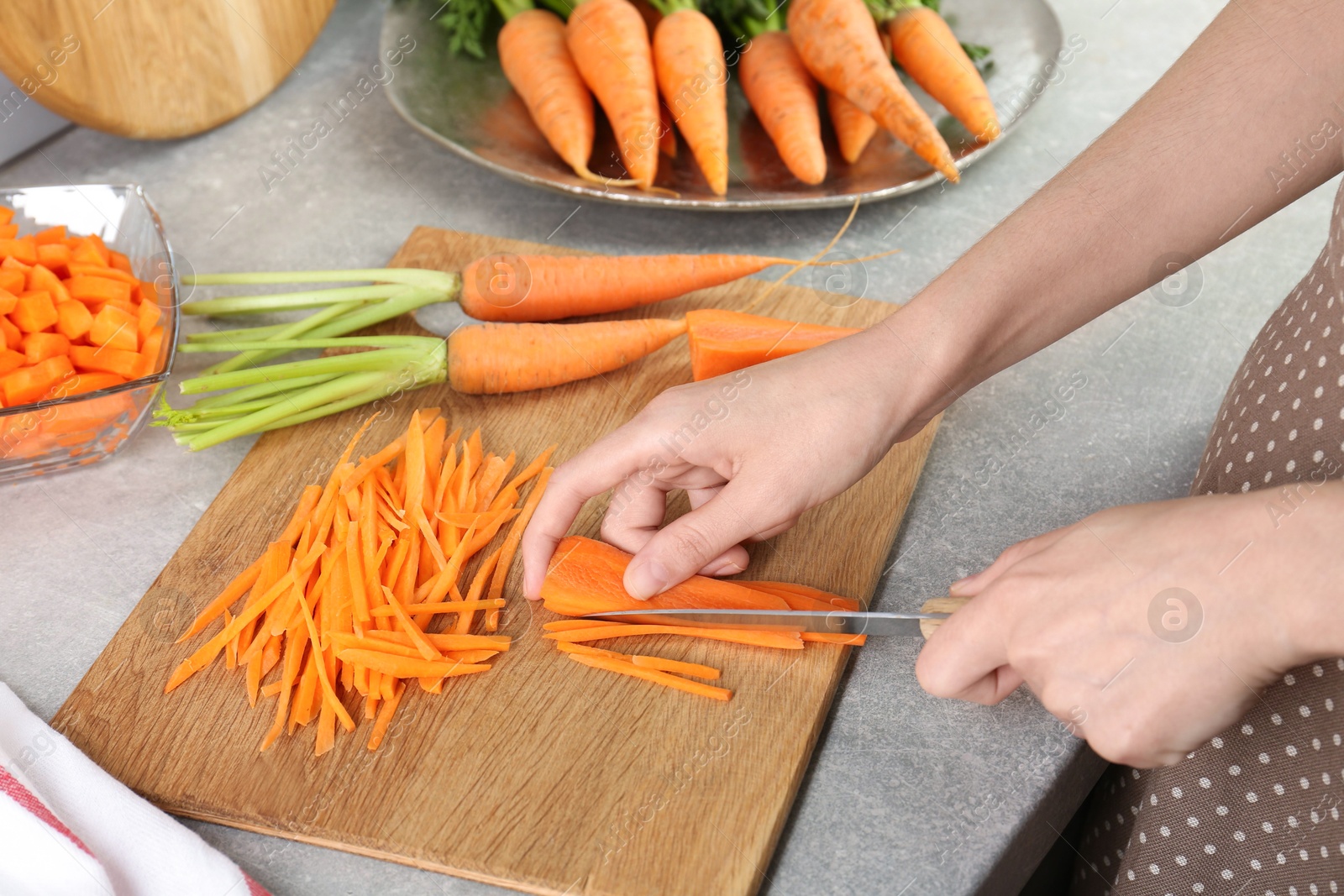 Photo of Woman cutting fresh carrot at gray textured table, closeup