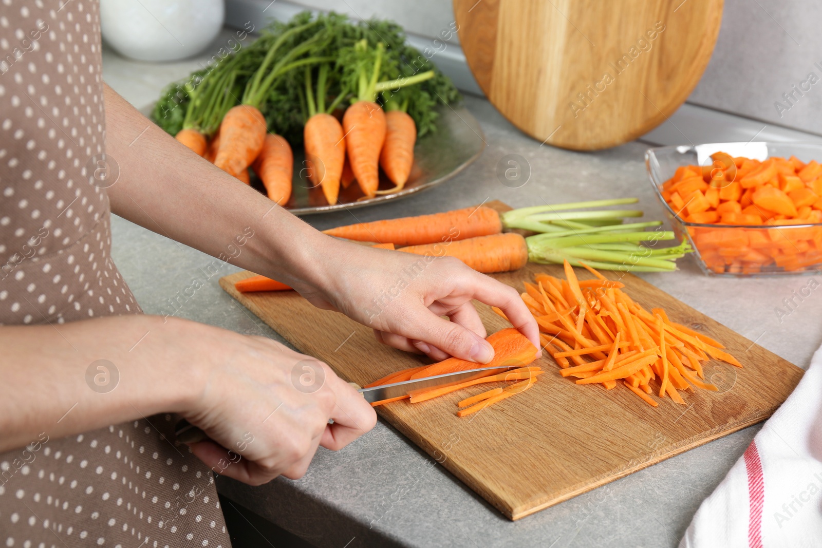 Photo of Woman cutting fresh carrot at gray textured table, closeup