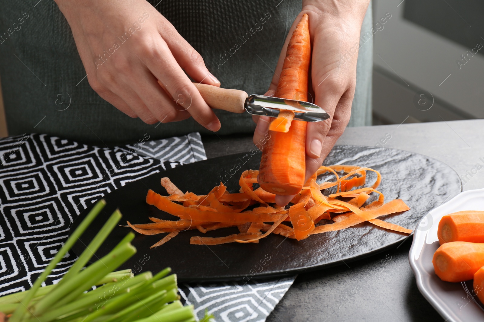 Photo of Woman peeling fresh carrot at dark gray table, closeup