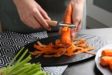 Photo of Woman peeling fresh carrot at dark gray table, closeup