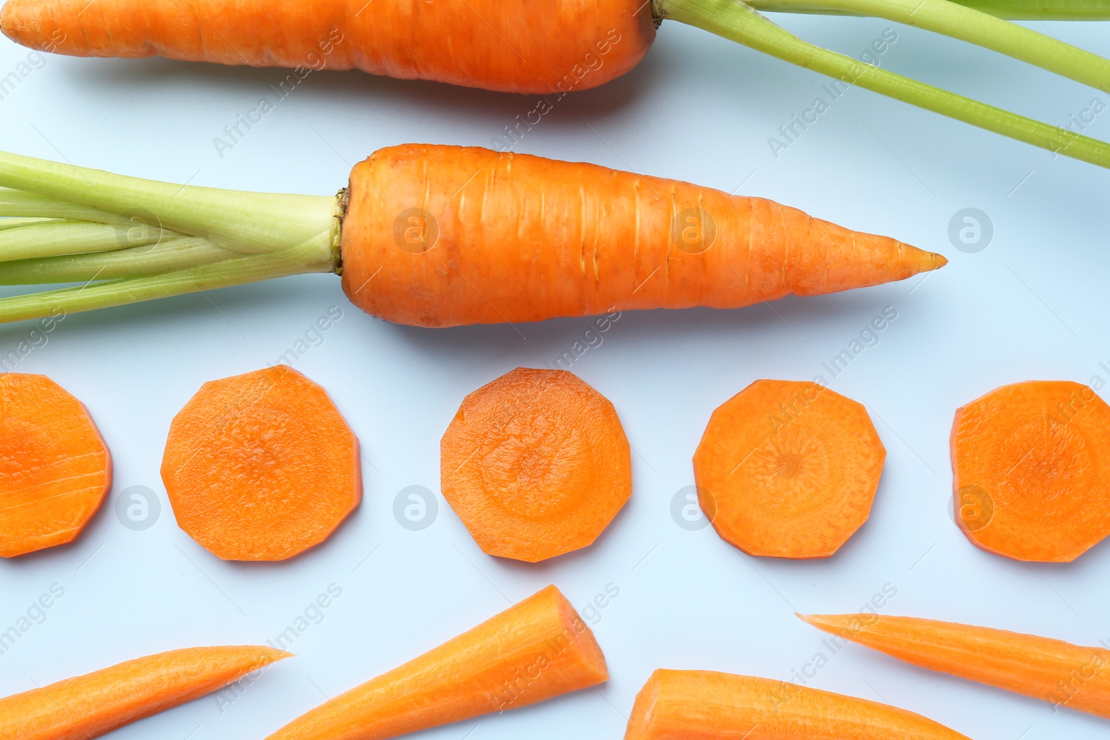 Photo of Whole and cut fresh carrots on light background, flat lay